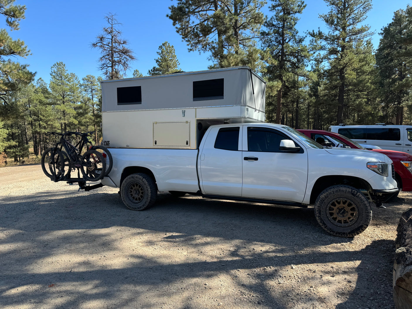 White pickup with an overland truck camper & bikes, perfect for an RV rental adventure in the woods.