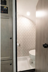 Compact RV rental wet bath with modern herringbone tile, toilet, and shower. Perfect for travel adventures.