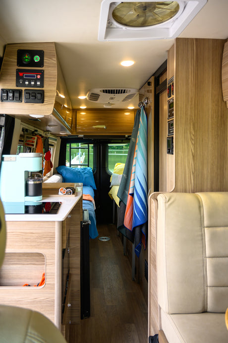Explore this cozy RV rental interior, showcasing a compact kitchen, essential controls, and a comfortable sleeping area.