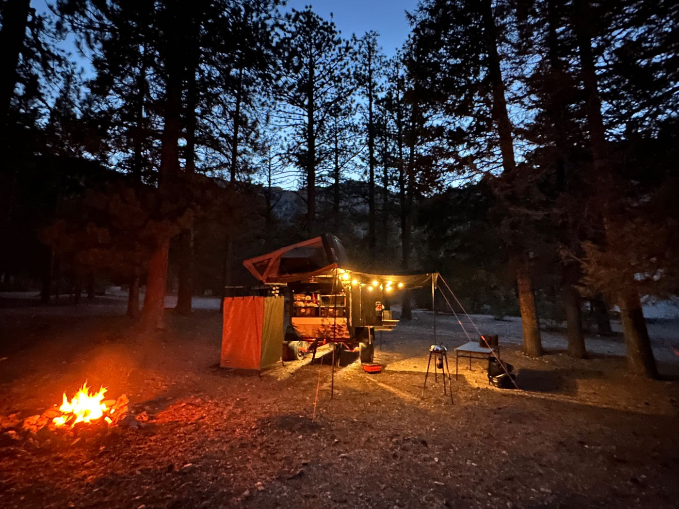 Cozy night camping. A bright campfire illuminates an RV rental trailer with a rooftop tent in a forested setting. — photo 17