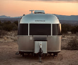RV rental: An Airstream travel trailer sits under a beautiful sunset sky, surrounded by mountains and desert landscape.