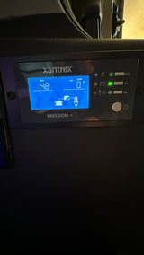 This Xantrex Freedom X inverter display in an RV rental shows 14.8V battery and 0W load, monitoring the electrical system in a camper.
