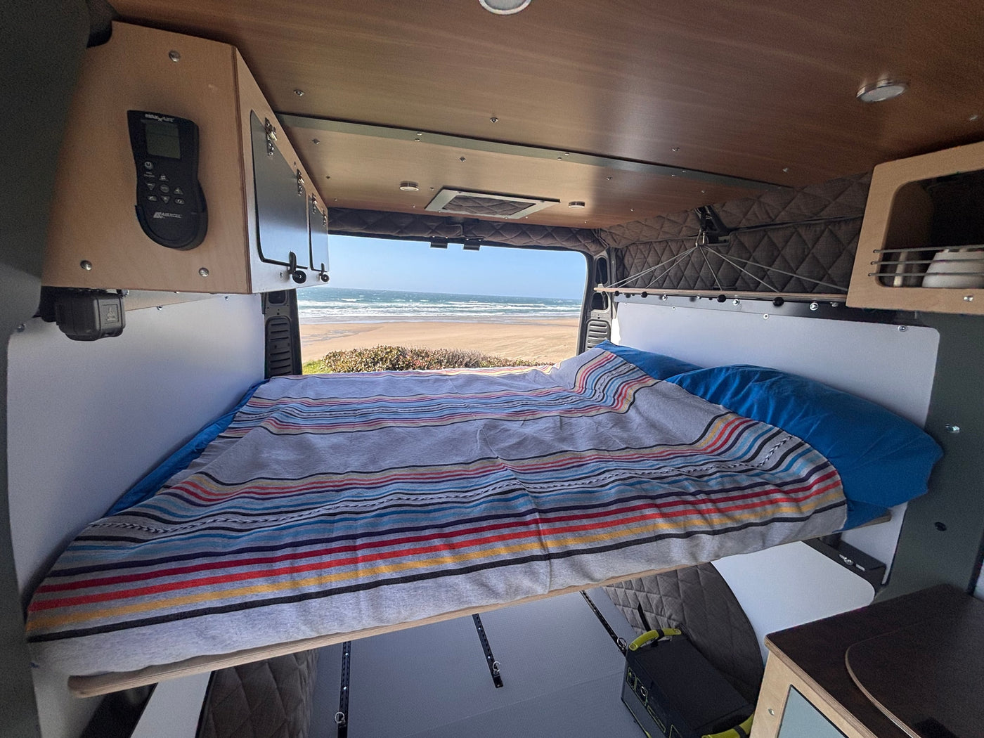 Inside a comfortable RV rental, a bed faces a stunning ocean view, offering a serene travel experience. — photo 3