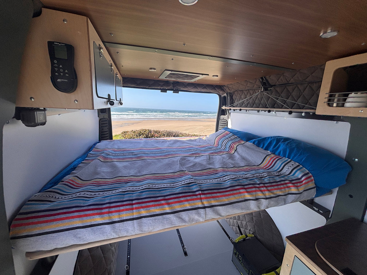 Inside a comfortable RV rental, a bed faces a stunning ocean view, offering a serene travel experience.