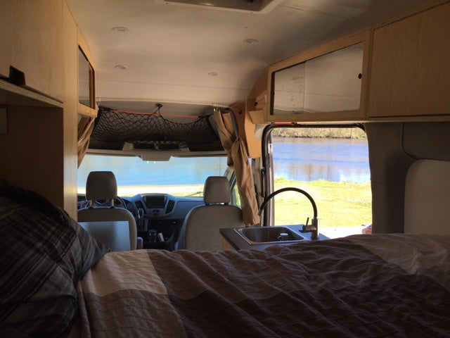 Cozy rv rental interior featuring a bed, sink, and a beautiful water view from inside the camper van.