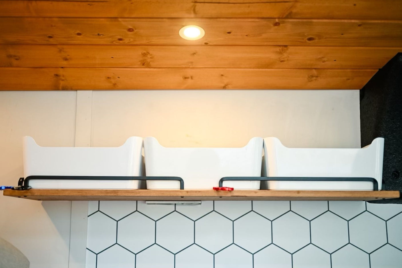 RV rental: Wooden ceiling, light, shelf with white storage bins, and hexagonal tile backsplash for efficient organization.