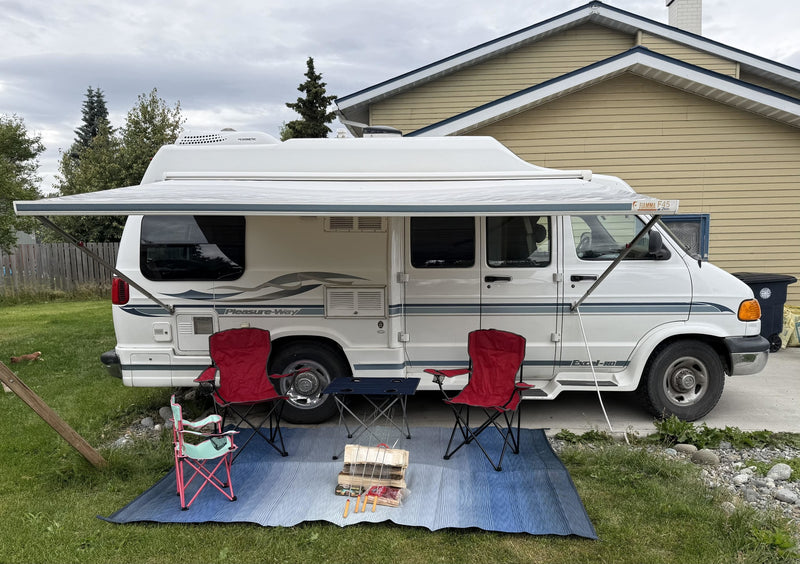White RV rental with awning extended. Camping chairs, table, and firewood on a blue outdoor mat, ready for use. — photo 2