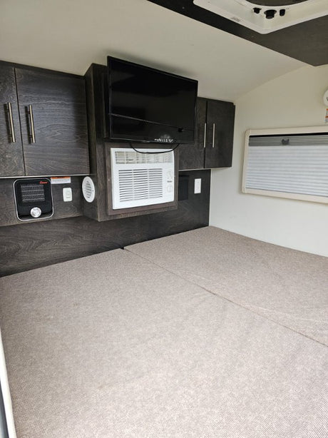 Experience an RV rental! Compact interior with bed, TV, AC unit, heater, and sleek storage cabinetry.