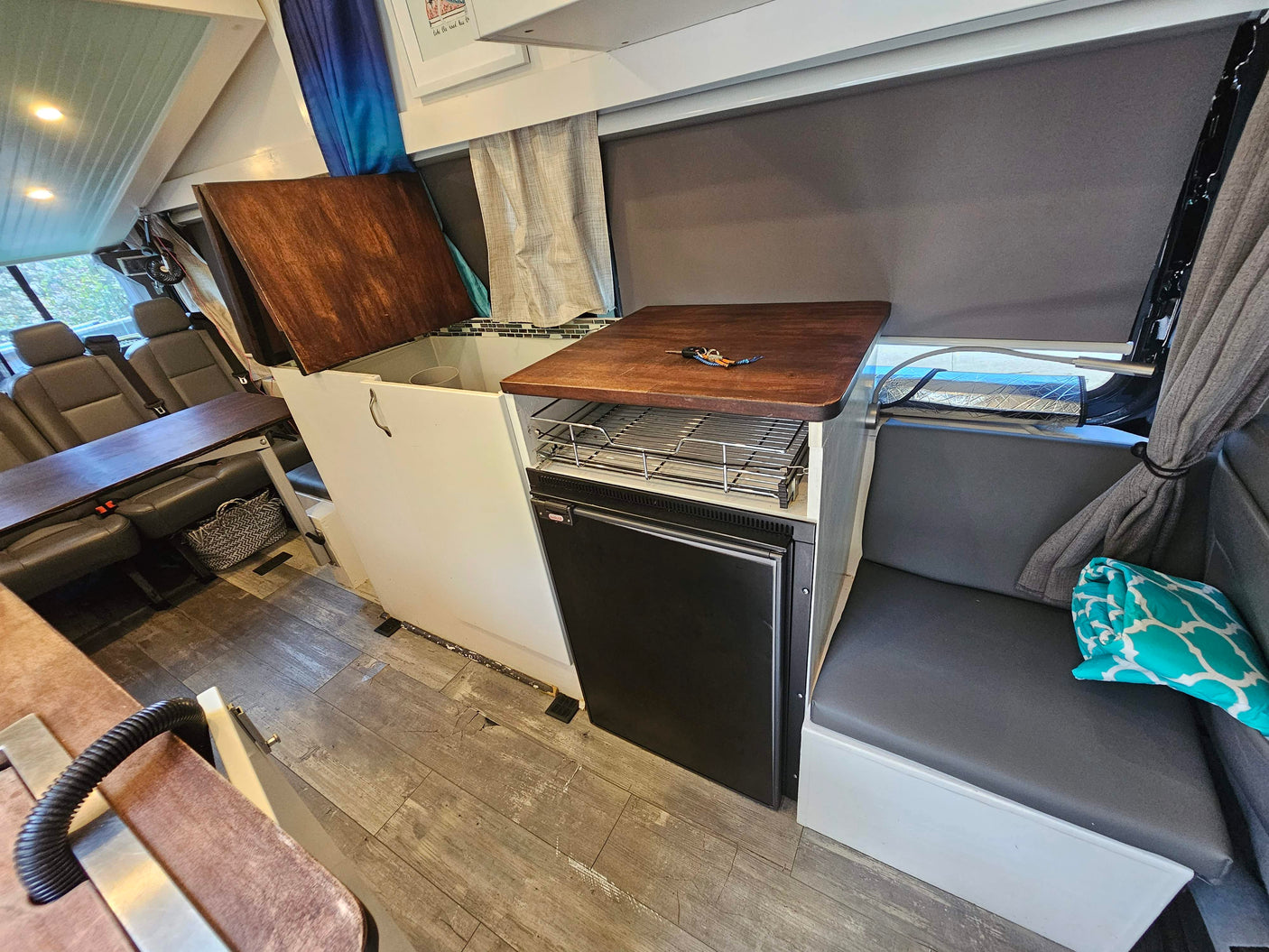 RV rental interior: kitchenette with sink/fridge, dinette table, and comfy bench seating on wood-look floor. Travel ready.