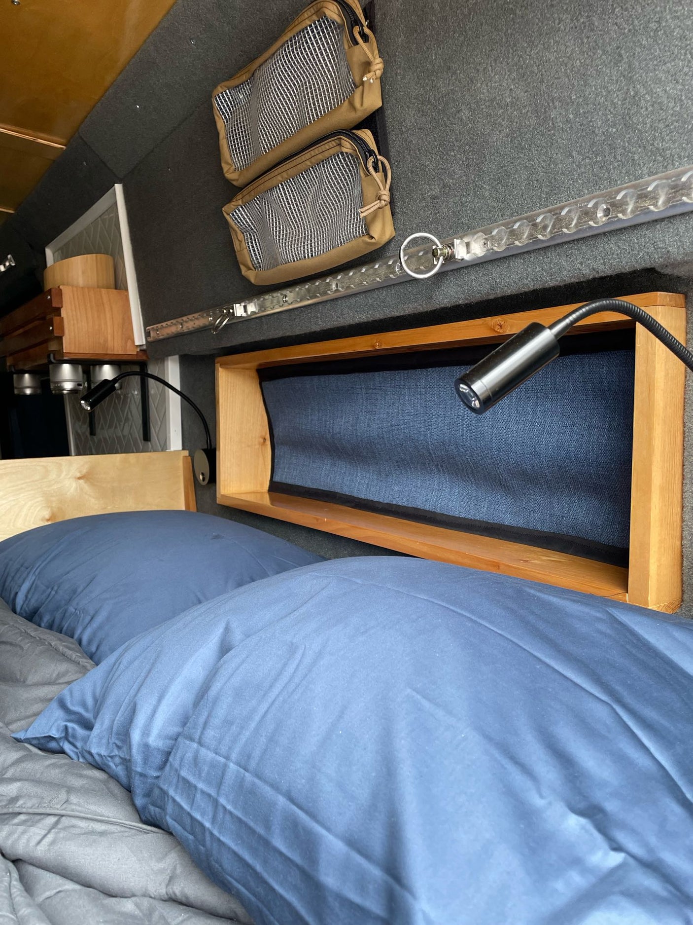 Inside an RV rental: a cozy bed with blue pillows, an adjustable reading lamp, and organized wall storage bags.