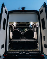 Rear view of a premium RV rental interior featuring black leather seating, a convertible bed, and elegant wood flooring under bright lights.