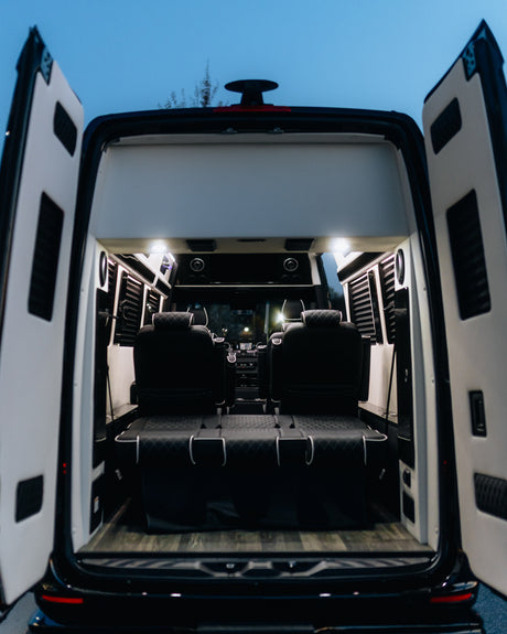 Rear view of a premium RV rental interior featuring black leather seating, a convertible bed, and elegant wood flooring under bright lights.