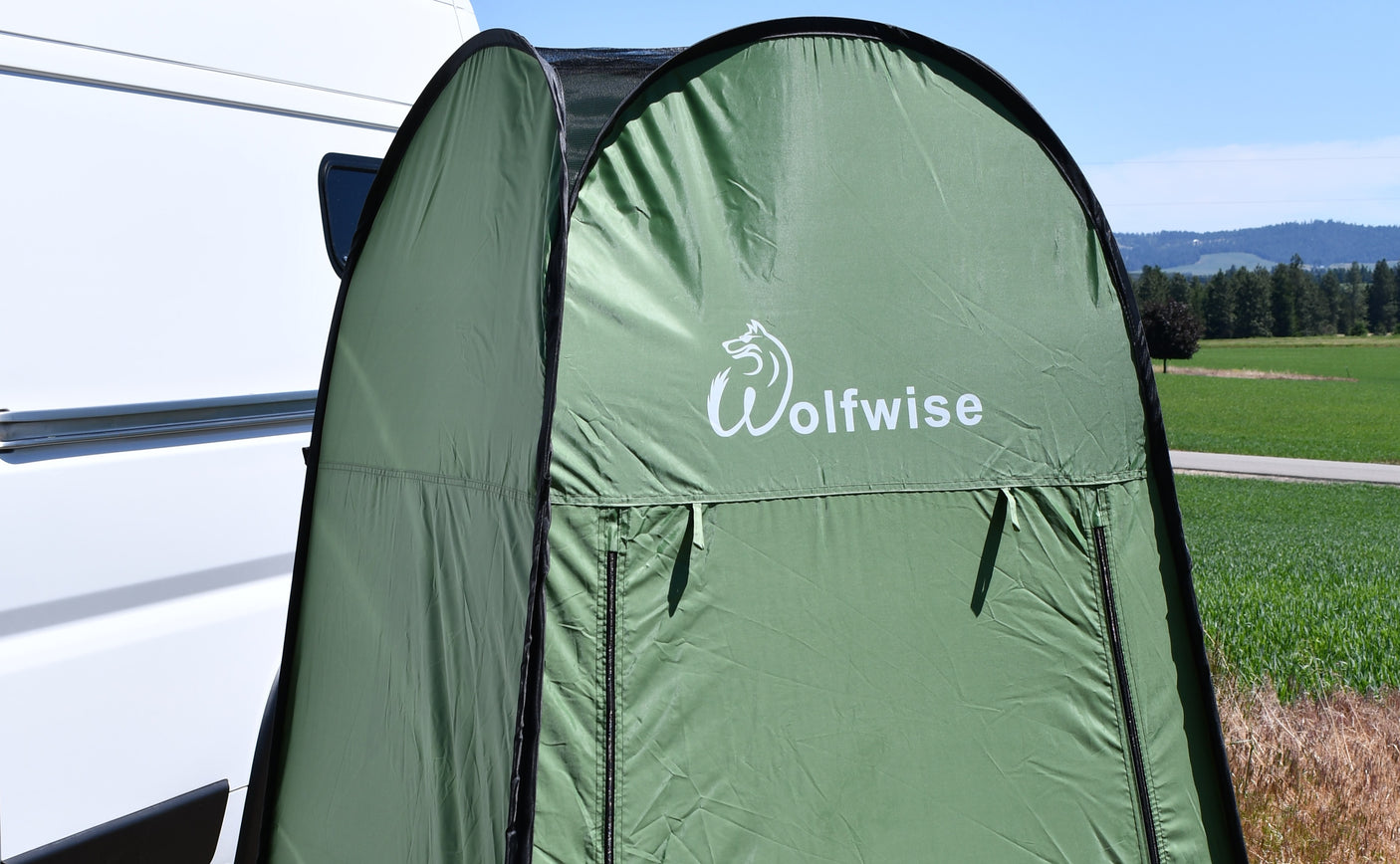 A green Wolfwise pop-up privacy tent stands beside a white RV, perfect for rv rental trips. Sunny outdoor camping scene.
