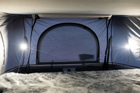 Inside an RV rental pop-top camper, a cozy bed, closed arched window, and bright lights create a comfortable space.