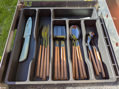 An RV rental's organized cutlery drawer: knives, forks, and spoons with wood handles and a green knife in a tray.