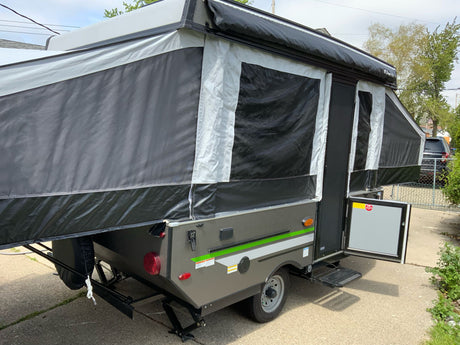 This fully extended pop-up RV rental, in black, grey, and white, features an open door and steps, parked on pavement.