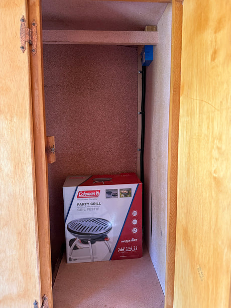 RV rental storage: A Coleman Party Grill box neatly fits in a compact cabinet, ideal for outdoor cooking on the go.
