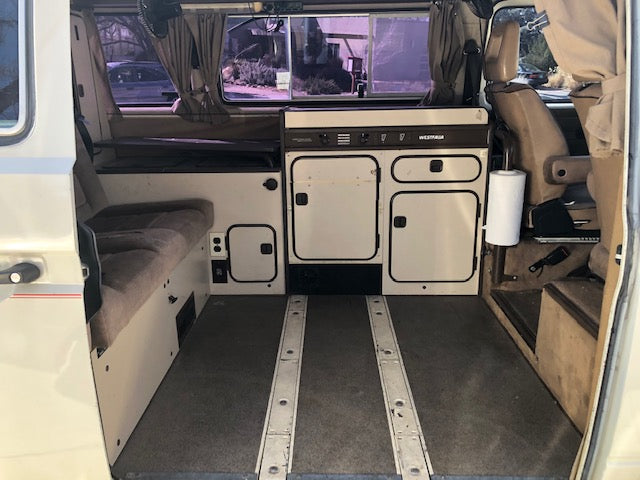 Inside this clean RV rental: a compact camper van kitchenette & living space with cozy seating.