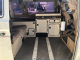 Inside this clean RV rental: a compact camper van kitchenette & living space with cozy seating.