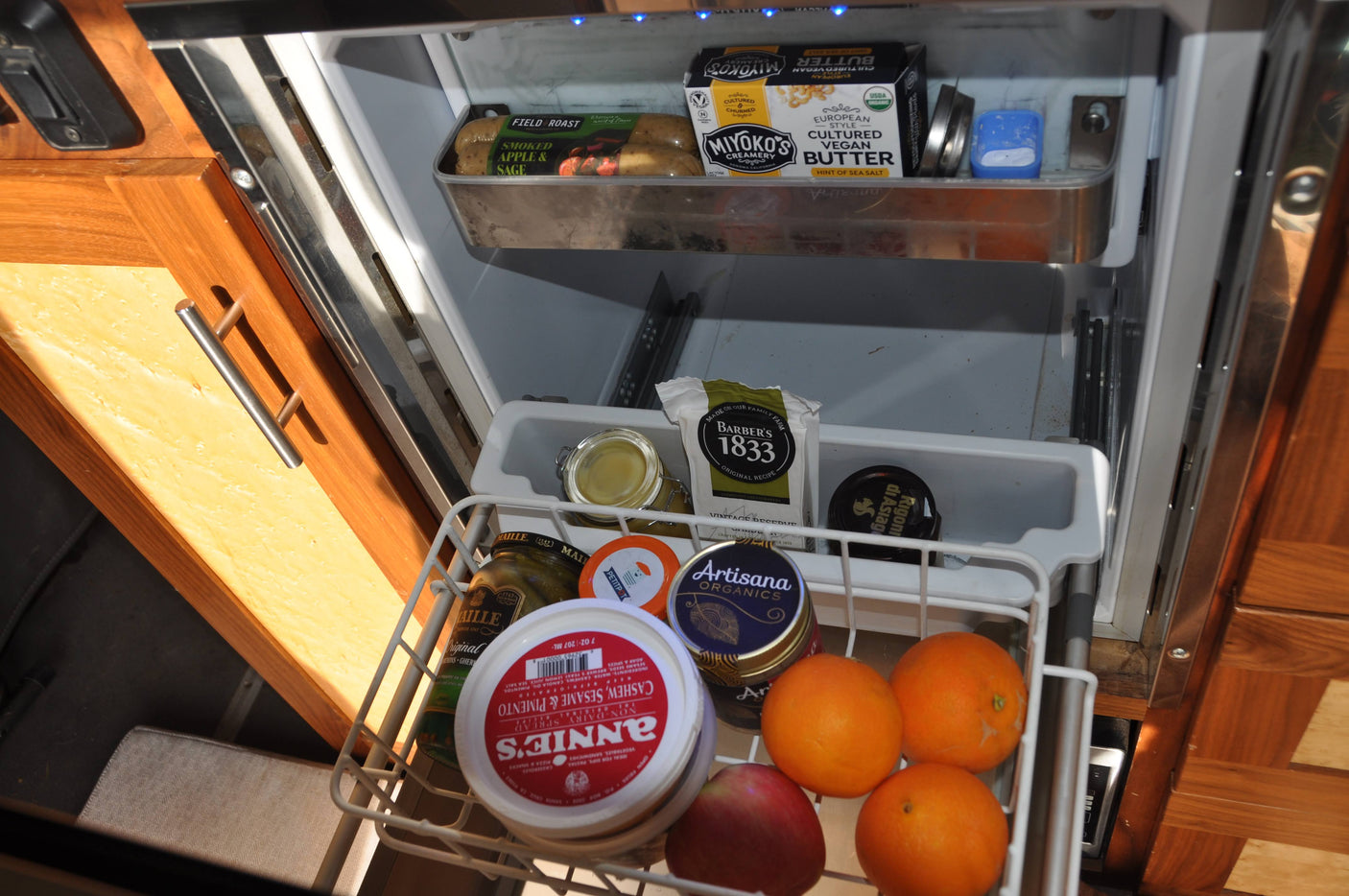 RV rental fridge stocked with vegan butter, sausages, cheese, fruits, and spreads in a convenient pull-out basket.