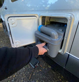 Emptying the RV rental's cassette toilet: A hand pulls the waste tank from its side compartment for disposal.