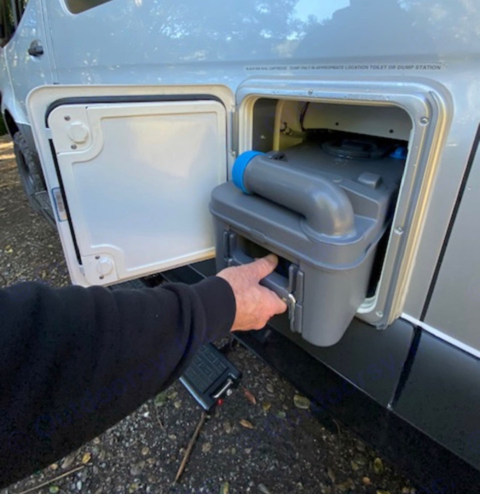 Emptying the RV rental's cassette toilet: A hand pulls the waste tank from its side compartment for disposal.