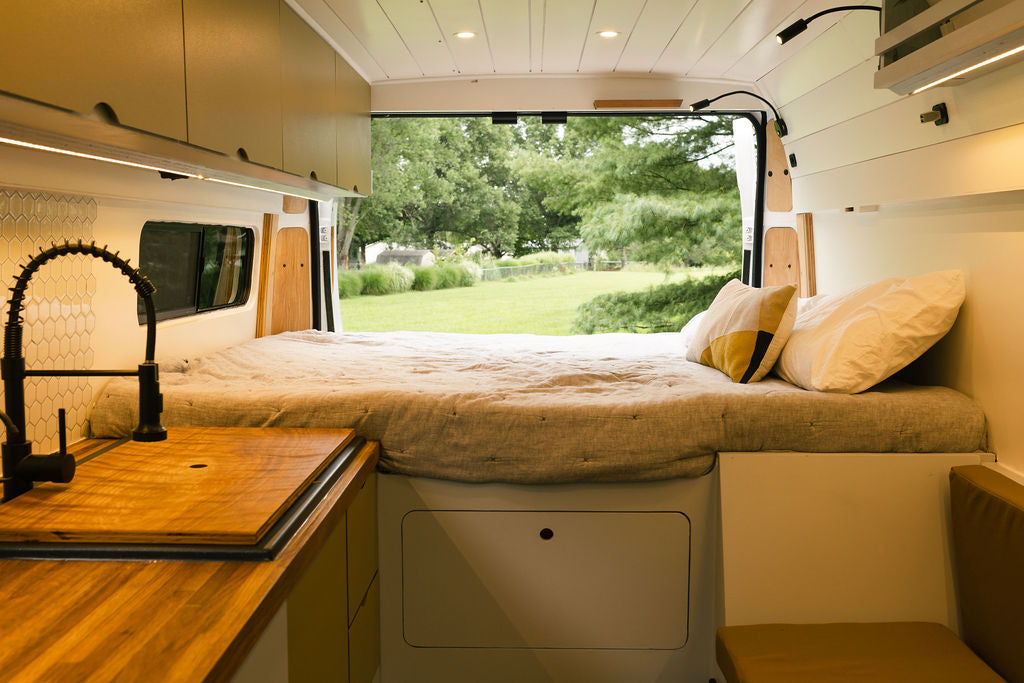 Step inside this RV rental: a comfy bed, kitchen, and expansive view out the back door into a lush green yard. — photo 14