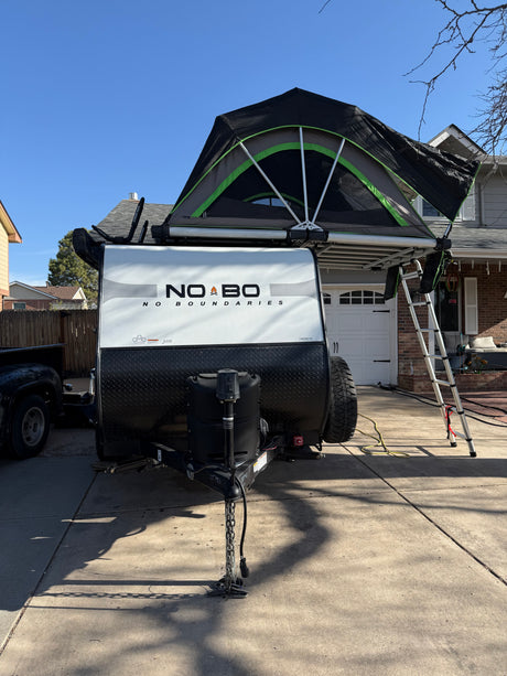 Experience outdoor adventure with this RV rental! A No Boundaries travel trailer with its rooftop tent and ladder set up.