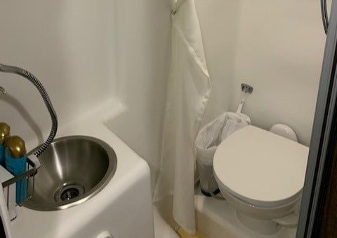 Compact RV rental wet bath. Features a sink with integrated shower, toilet, and curtain for efficient space use.