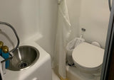 Compact RV rental wet bath. Features a sink with integrated shower, toilet, and curtain for efficient space use.