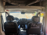 View of an RV rental van's front cabin from the back, highlighting seats, dashboard, and the road ahead.
