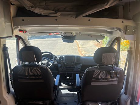 View of an RV rental van's front cabin from the back, highlighting seats, dashboard, and the road ahead.