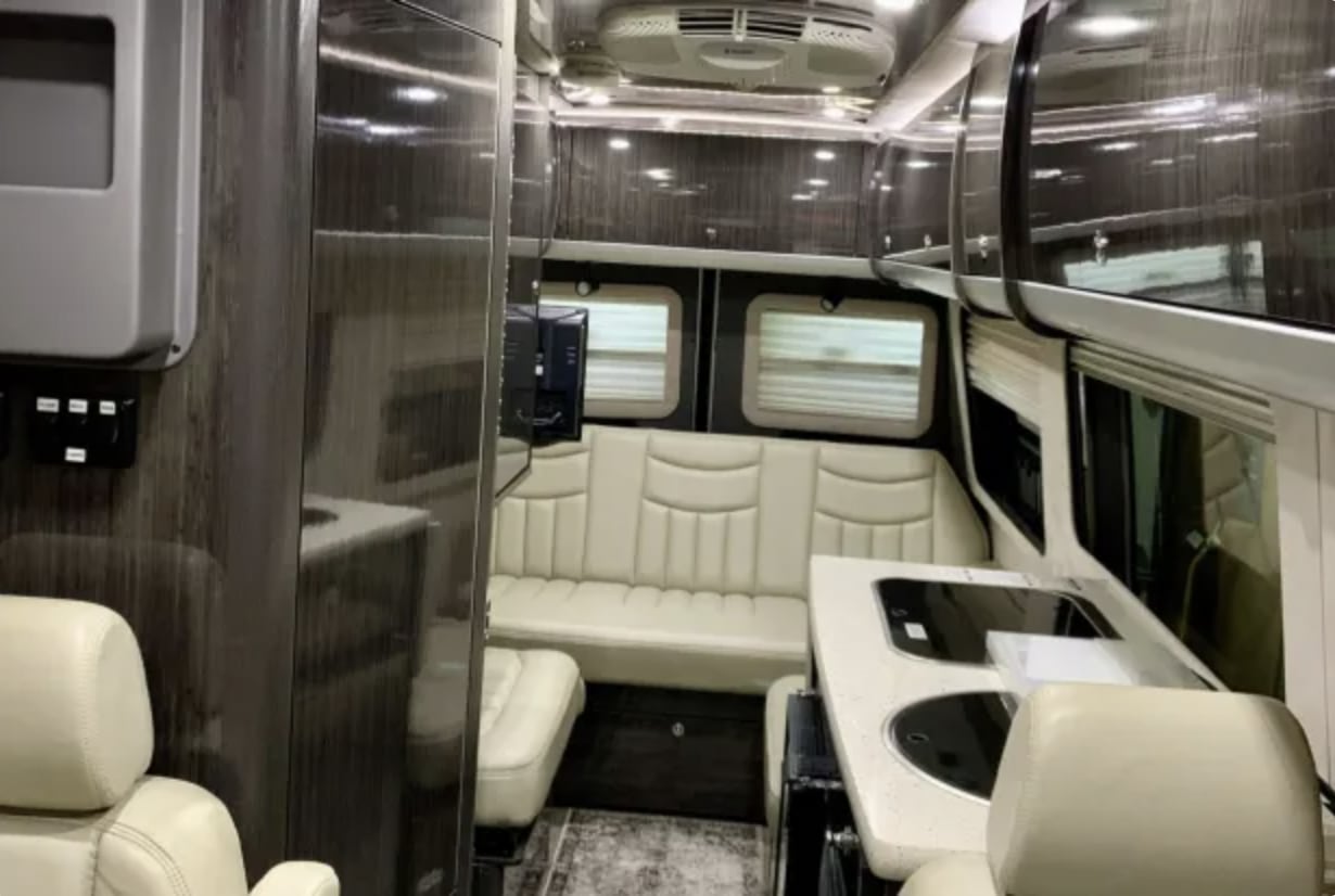 RV rental: Modern camper van interior with cream leather seating, a compact kitchen, overhead storage, and a TV.