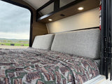 Cozy RV rental interior with a made bed and scenic outdoor views from the window. Perfect for mobile adventures.