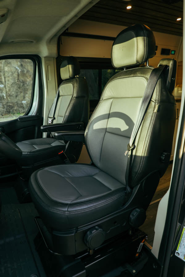 Inside this RV rental: Comfortable black and light grey leather driver and passenger seats, ready for your adventure.