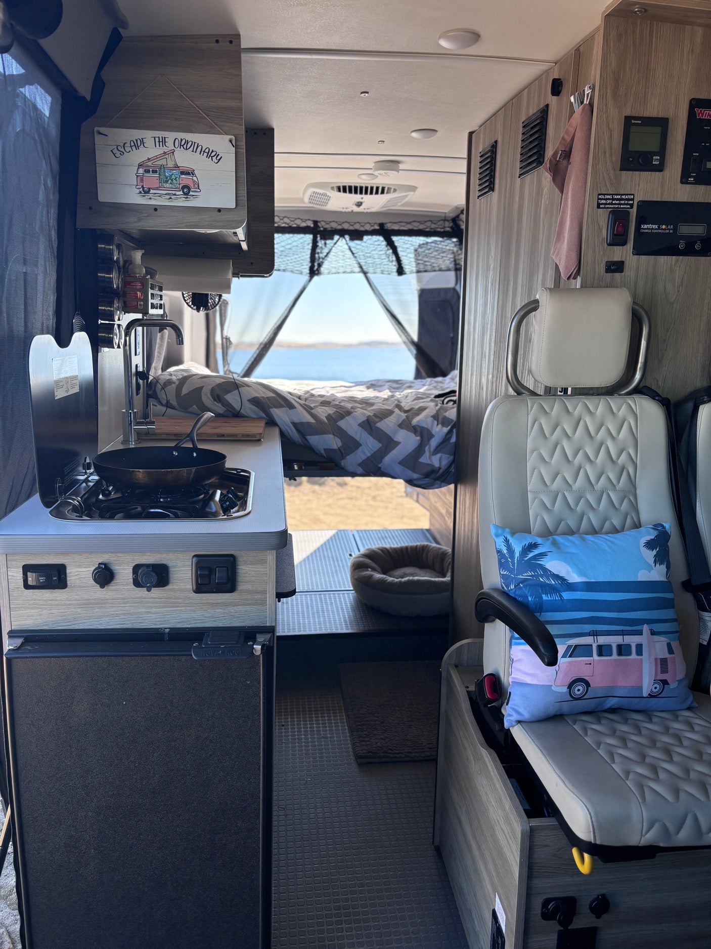 Explore this RV rental: compact kitchen, cozy bed with a scenic lake view, and a small lounge area inside.