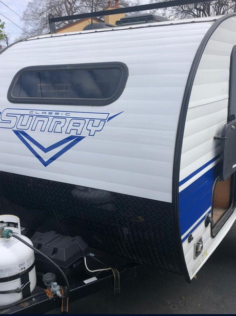 Front side of a white SunRay Classic travel trailer with blue accents, ideal for rv rental. Propane tank in view.