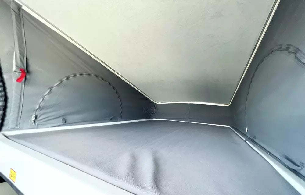 Inside a pop-top RV rental: gray fabric tent-like walls, light ceiling, and a comfortable sleeping platform for camper adventures.