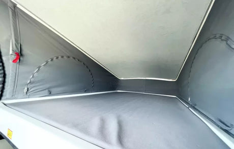 Inside a pop-top RV rental: gray fabric tent-like walls, light ceiling, and a comfortable sleeping platform for camper adventures.