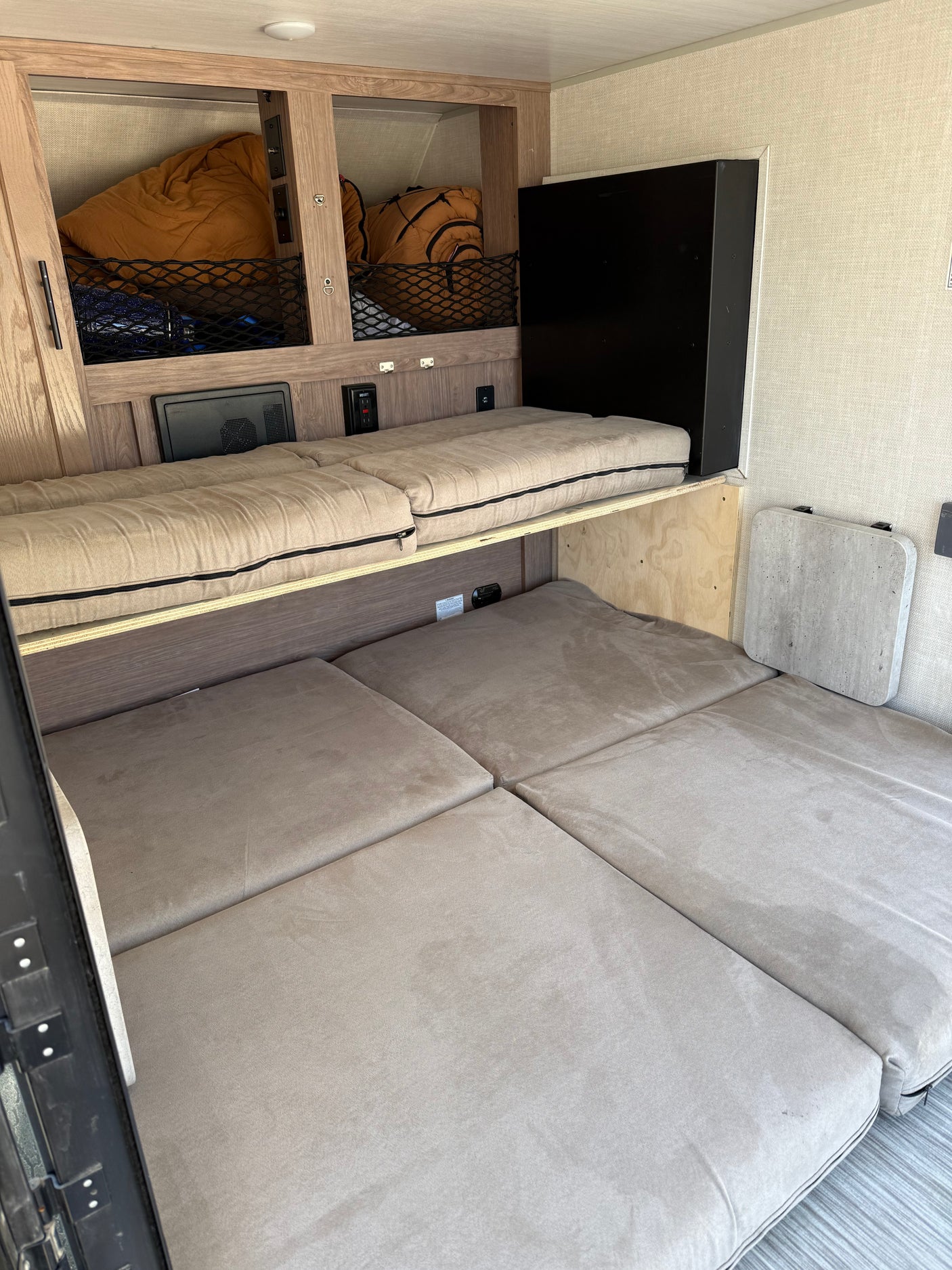 RV rental interior featuring upper and lower bunk beds, built-in storage nets, and a wall-mounted table.