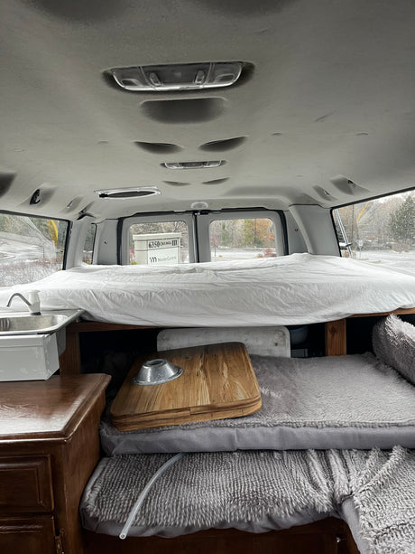 Cozy RV rental interior: bed, sink, and storage in a custom camper van conversion. Perfect for mobile living.