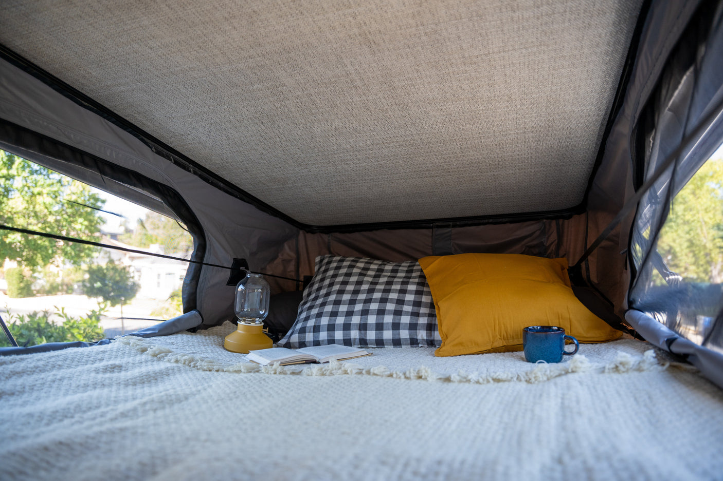 Cozy RV rental interior with comfy bed, pillows, book, and lantern. Perfect for a comfortable glamping adventure.