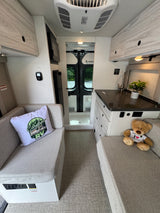 Cozy RV rental interior with light wood finishes, a compact kitchen, comfortable seating, and rear doors for scenic views.