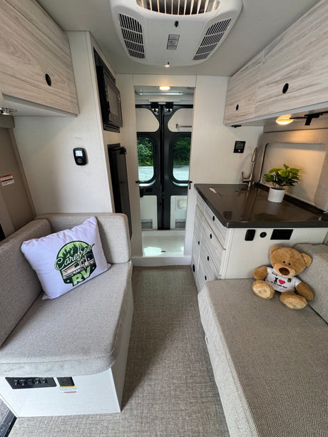 Cozy RV rental interior with light wood finishes, a compact kitchen, comfortable seating, and rear doors for scenic views.