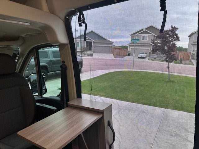 RV rental interior showing a functional table, front seats, and a clear view of a suburban neighborhood through a window screen.