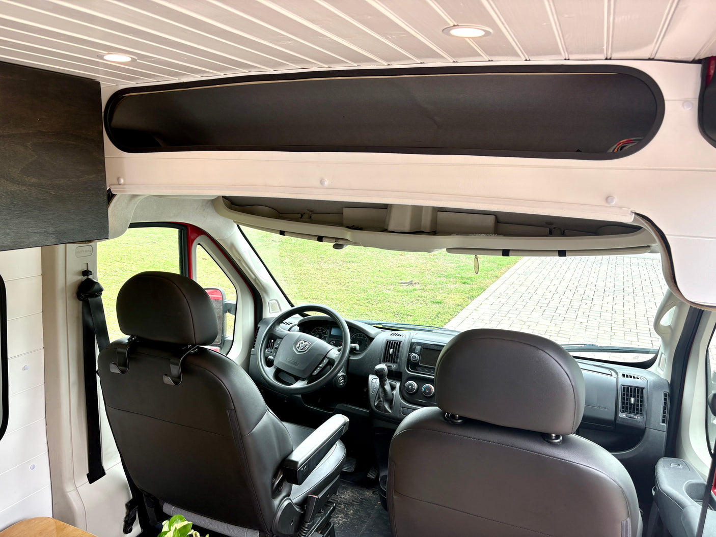 View inside an rv rental camper van: driver's cabin, custom overhead storage, and slatted white ceiling with lights.