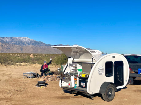 Enjoying the outdoors with an RV rental! This teardrop trailer offers a convenient kitchenette for desert camping near snowy mountains.