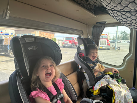 Happy kids in their car seats inside an RV rental, stopped at a gas station.
