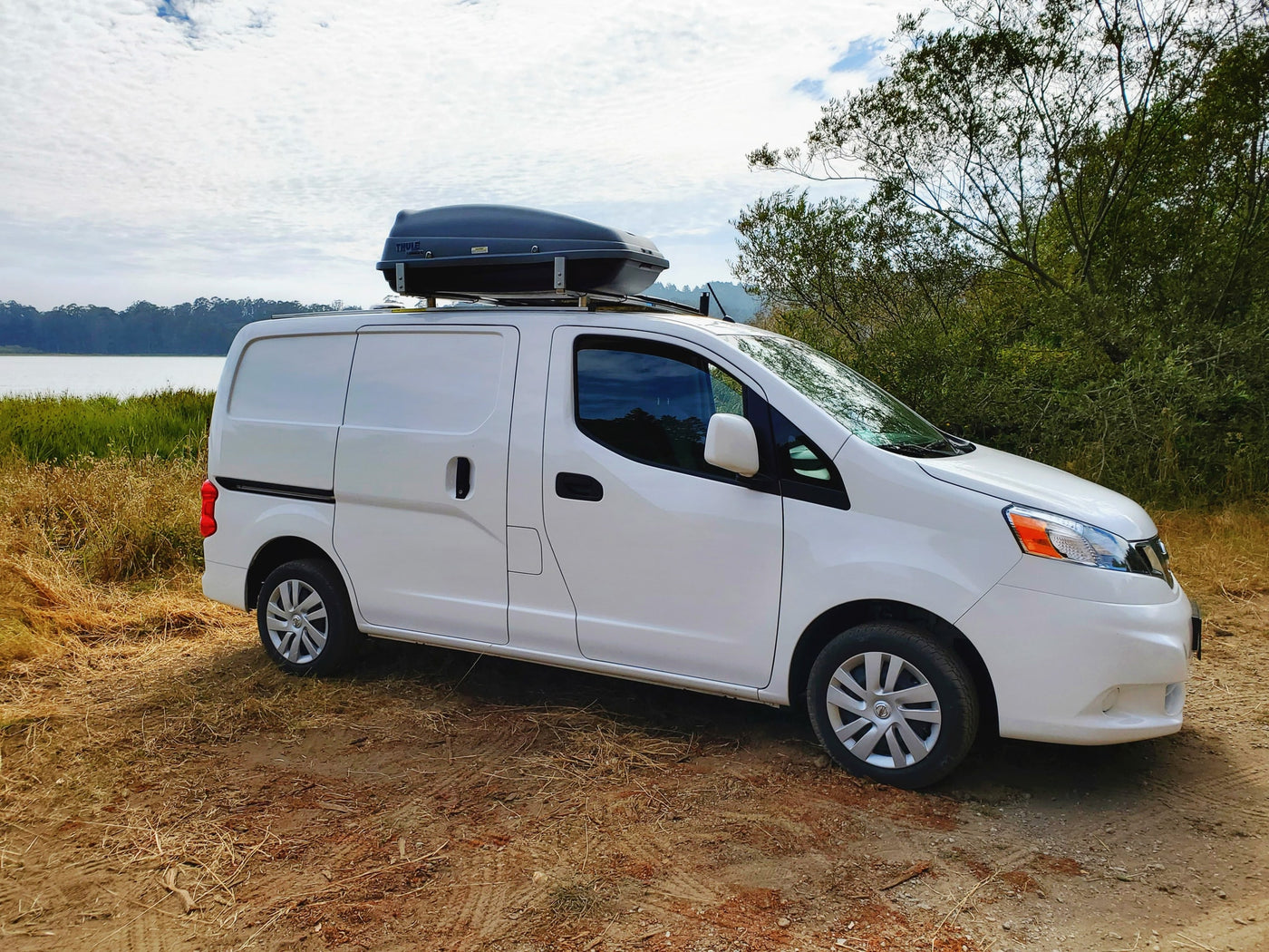 RV rental white van with roof box parked by a lake and trees on a sunny day. — photo 11