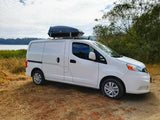 RV rental white van with roof box parked by a lake and trees on a sunny day.